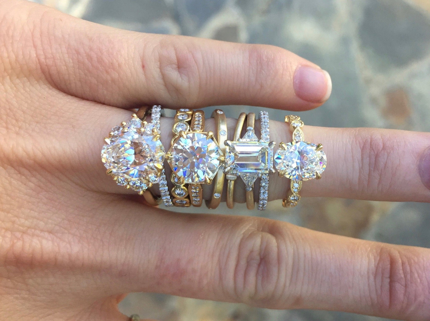 Stack of gold and diamond rings on a finger with a blurred natural background